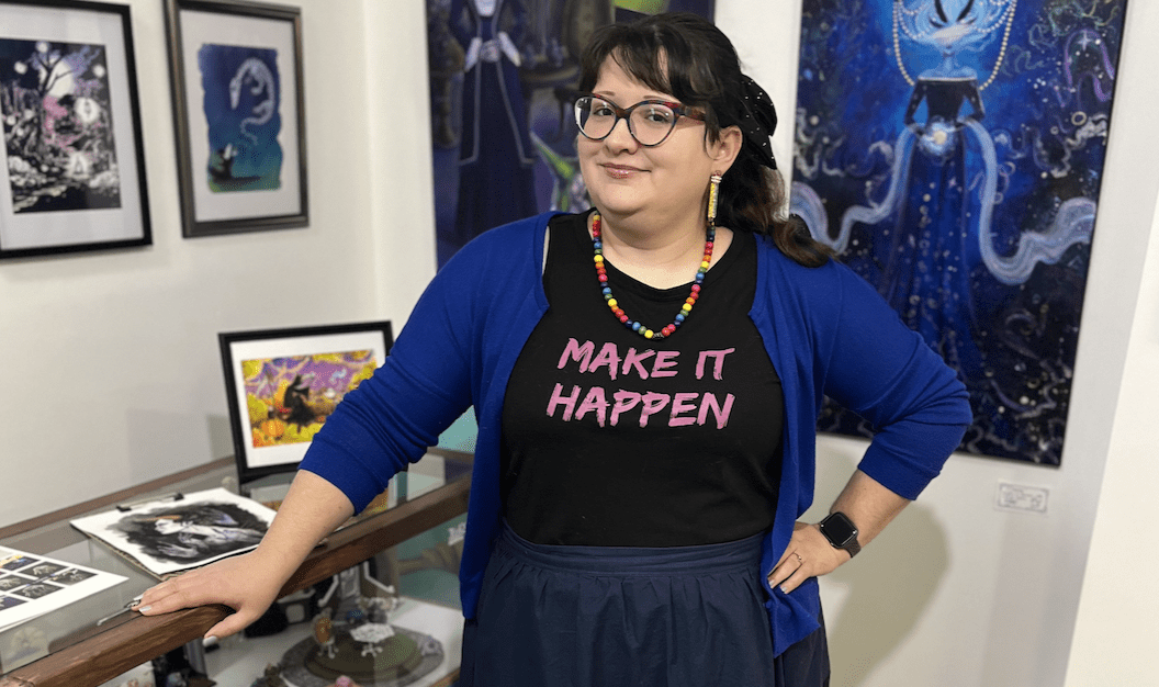 Audra Balion stands in her downtown studio, smiling, wearing a shirt that reads "Make it happen"